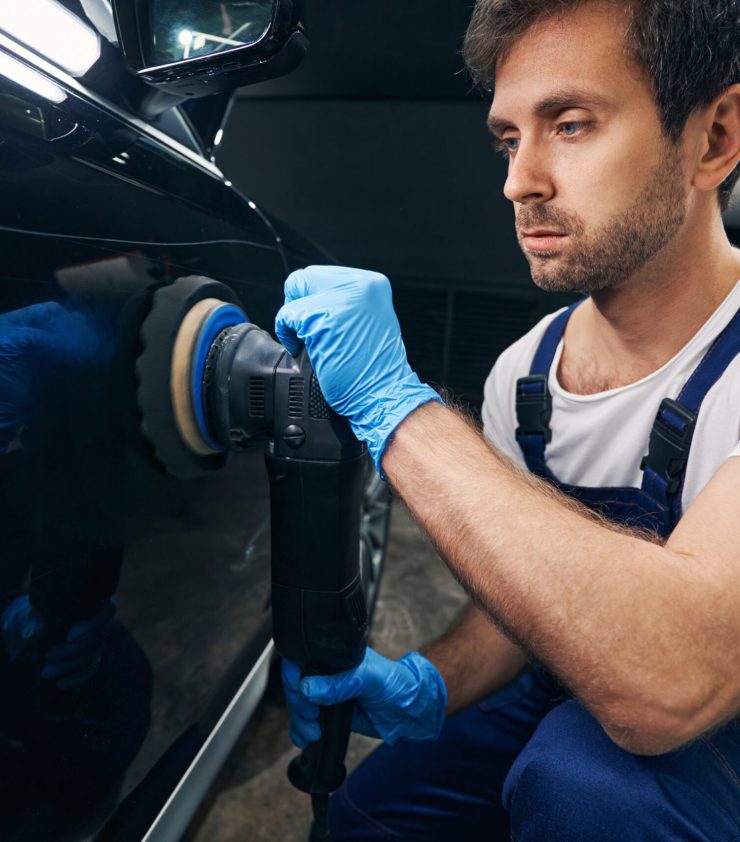 Man car mechanic moving polishing machine with soft felt pad along automobile body surface
